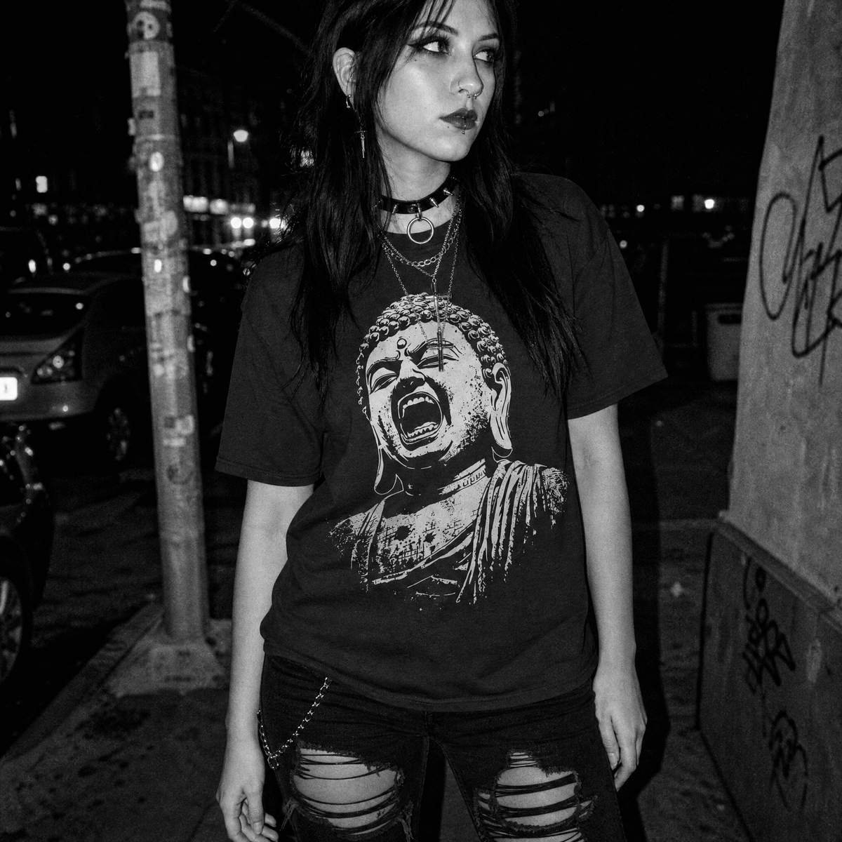 A woman wearing a black graphic t-shirt with a screaming Buddha print, photographed in a black and white street setting at night.