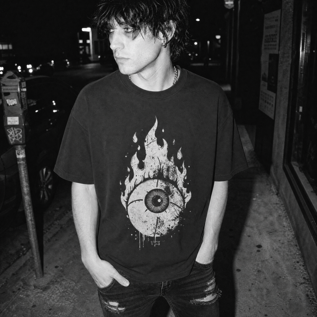 A black graphic t-shirt featuring a distressed white print of a burning eyeball, worn by a male in a black-and-white street photograph.