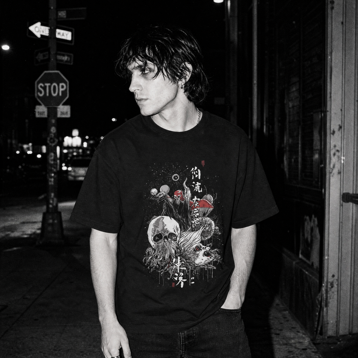 A man wearing a black graphic t-shirt with a detailed cosmic war design, standing on a city street at night.
