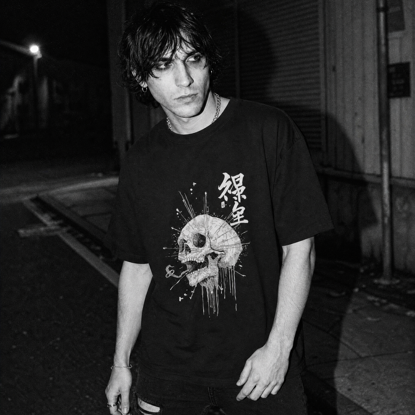 A black graphic t-shirt with a skull and Kanji characters, worn by a man standing on a dark street at night.