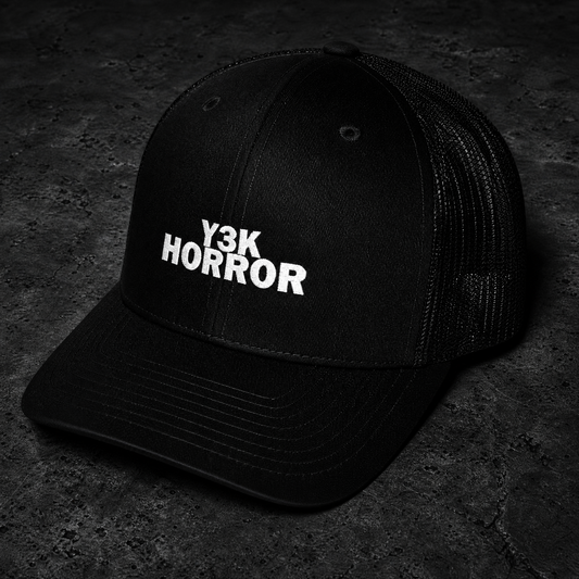 A black trucker-style cap with white embroidered text reading 'Y3K HORROR' on the front, photographed on a dark textured surface.